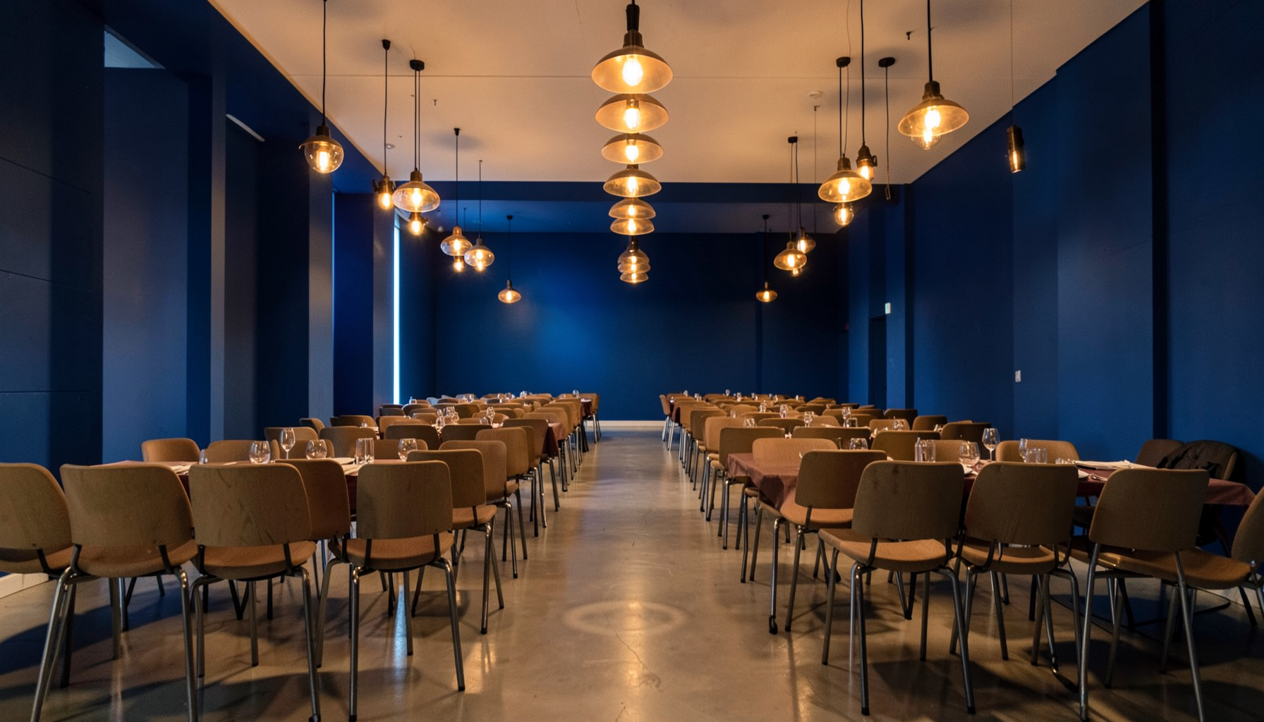 Warmly lit gathering space with rows of chairs and soft amber pendant lighting, evoking a community networking event atmosphere.